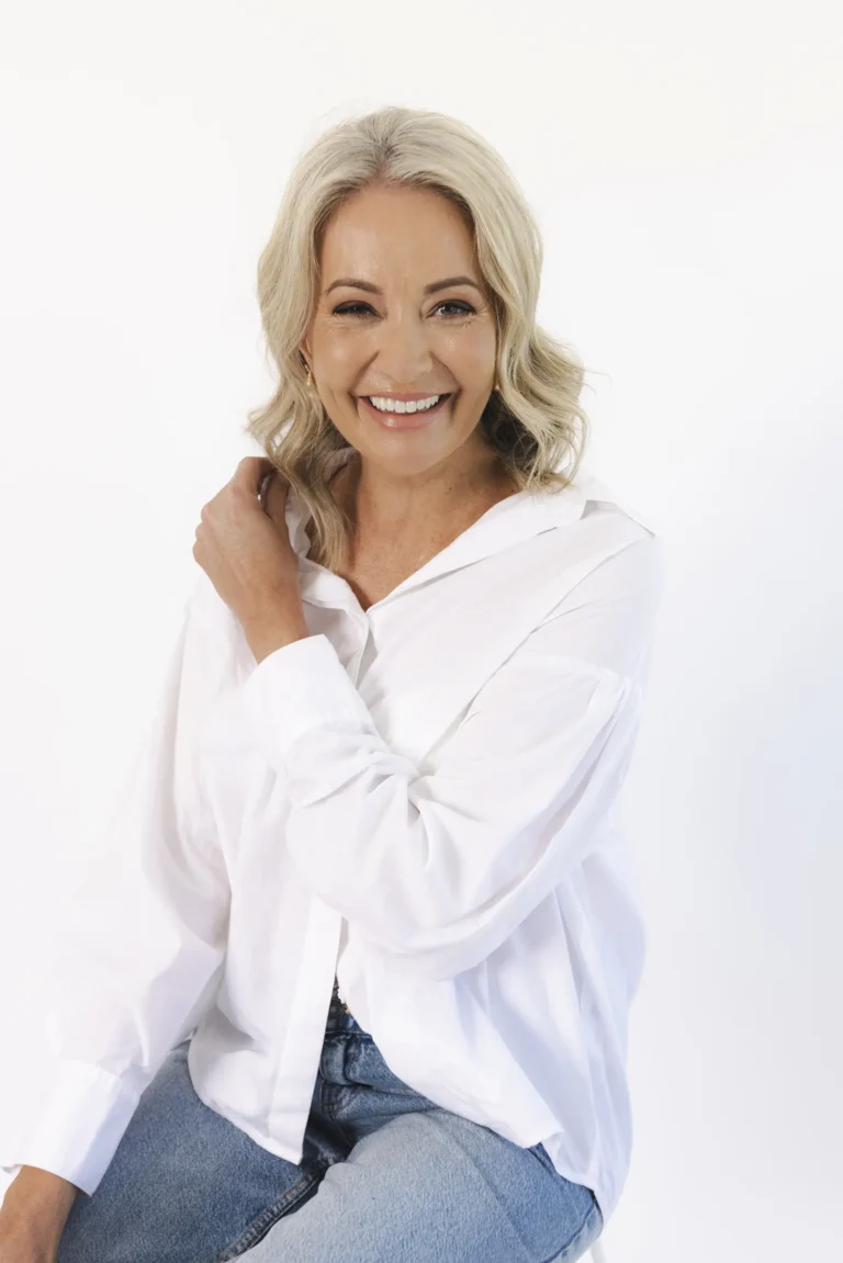 Danica Bunch wearing a white shirt and light blue jeans. She has long wavy blonde hair and is laughing and looking towards the camera.