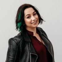 Headshot of a woman with short choppy black and green hair and a black leather jacket.